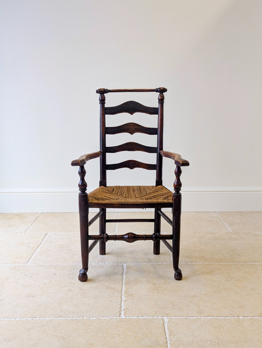 A late nineteenth-century country ash armchair featuring a ladderback design with four curved horizontal slats, turned armrest supports, and a hand-woven natural rush seat. View II