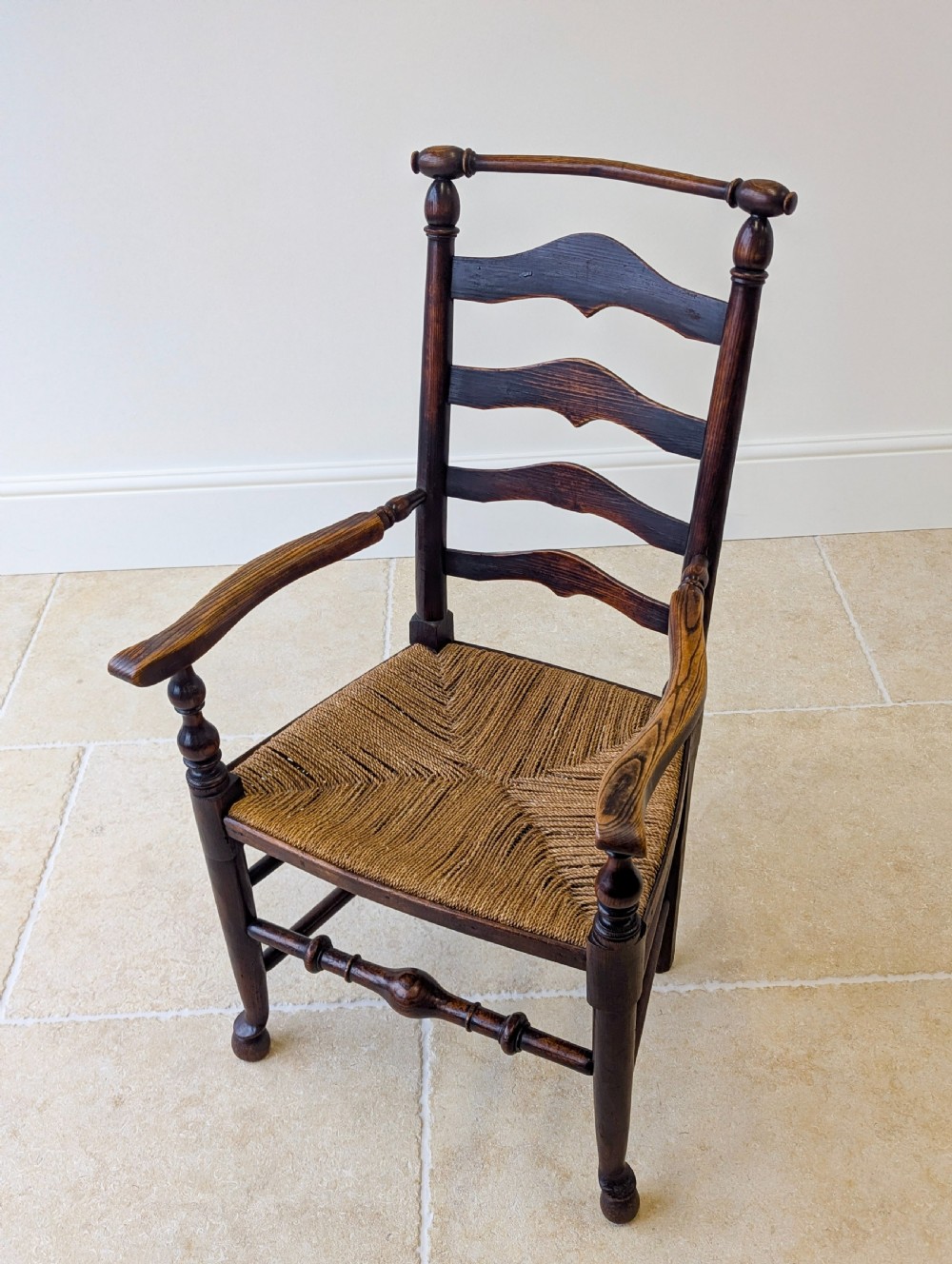 A late nineteenth-century country ash armchair featuring a ladderback design with four curved horizontal slats, turned armrest supports, and a hand-woven natural rush seat. View III