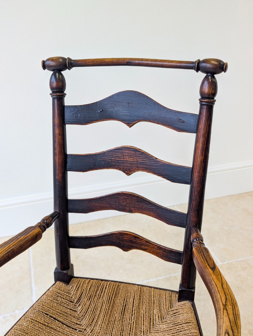 A late nineteenth-century country ash armchair featuring a ladderback design with four curved horizontal slats, turned armrest supports, and a hand-woven natural rush seat. View IV