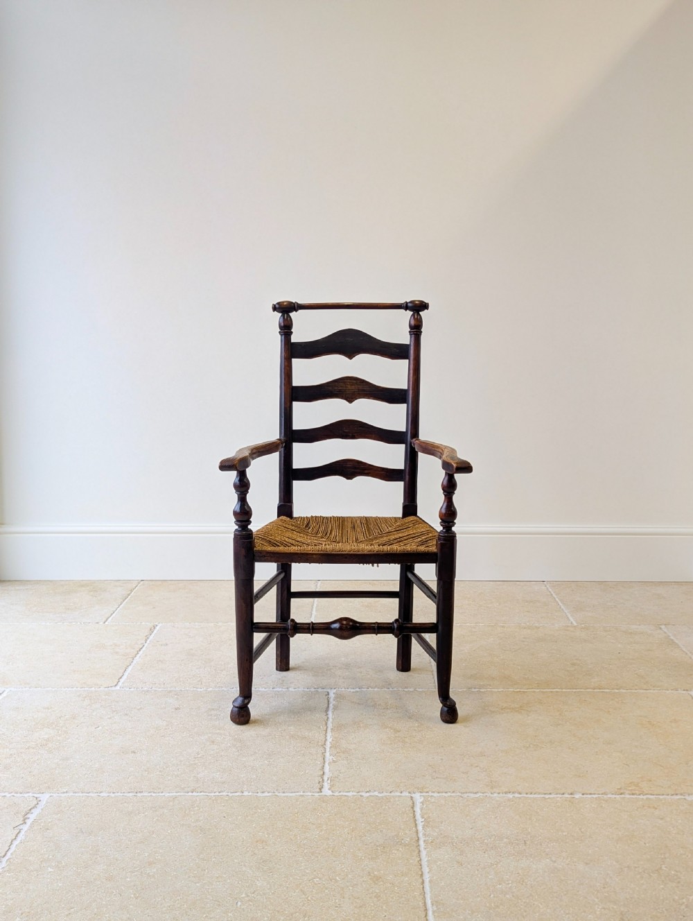 A late nineteenth-century country ash armchair featuring a ladderback design with four curved horizontal slats, turned armrest supports, and a hand-woven natural rush seat. View V