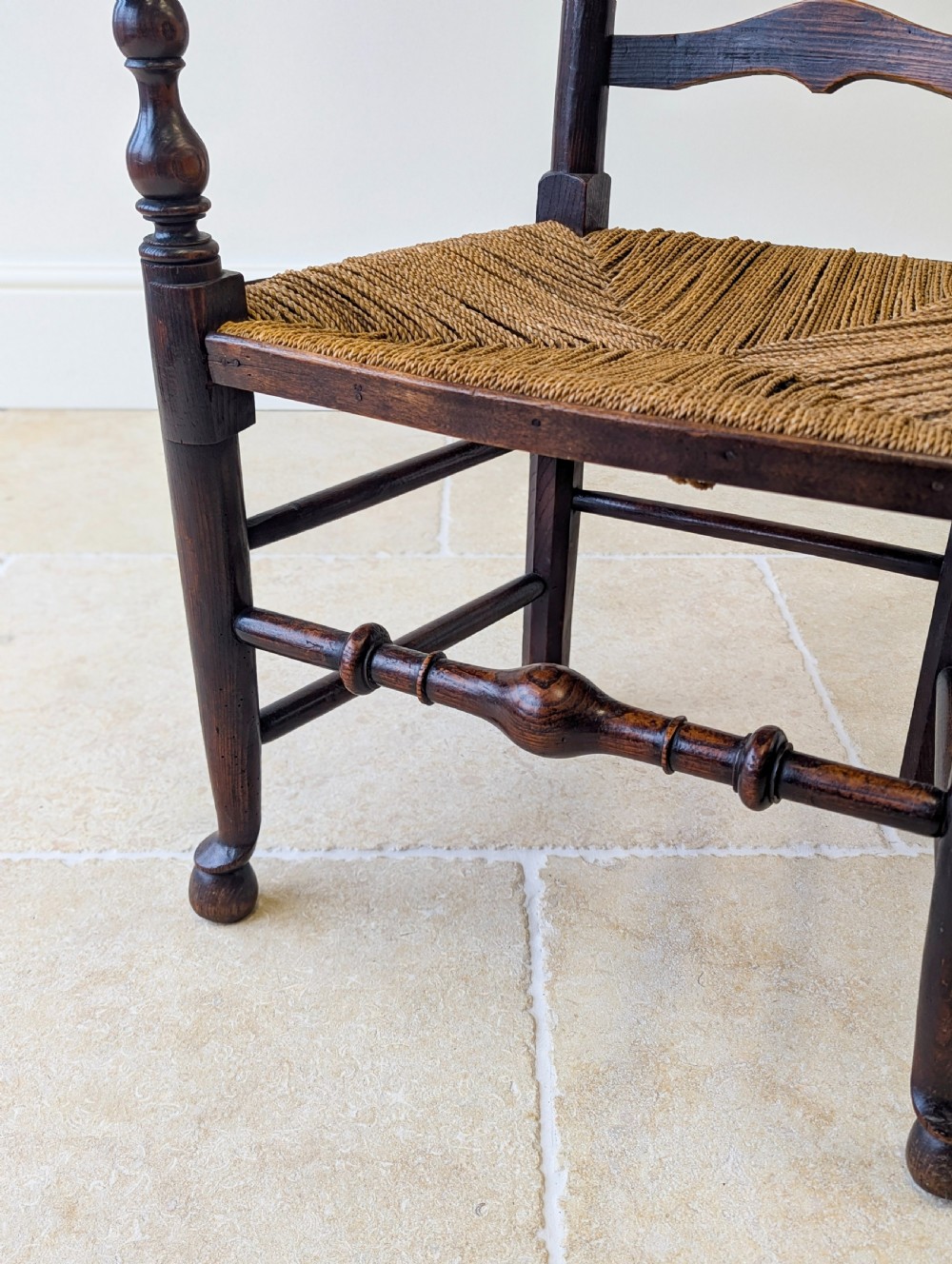 A late nineteenth-century country ash armchair featuring a ladderback design with four curved horizontal slats, turned armrest supports, and a hand-woven natural rush seat. View VI