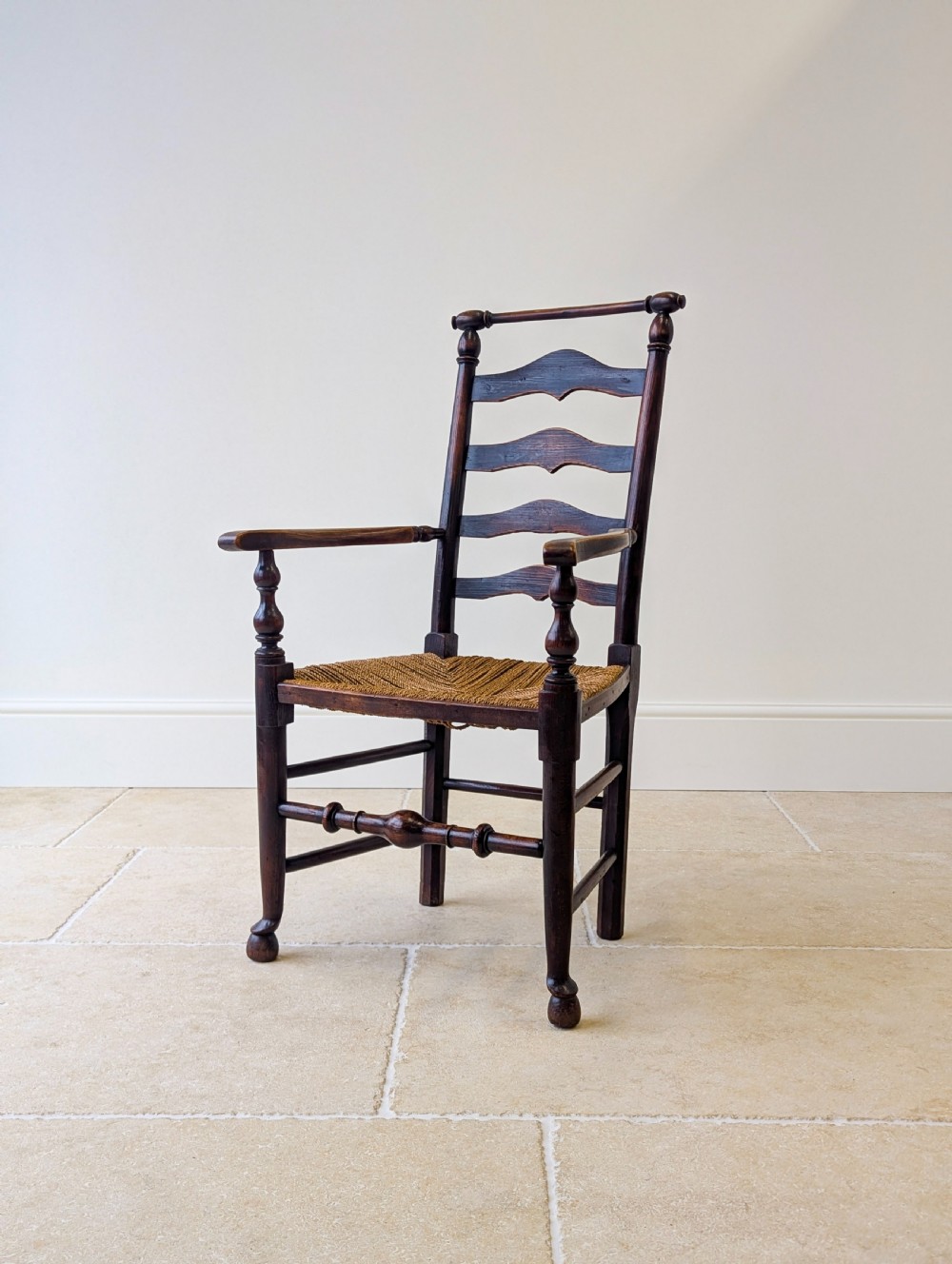 A late nineteenth-century country ash armchair featuring a ladderback design with four curved horizontal slats, turned armrest supports, and a hand-woven natural rush seat. View VII