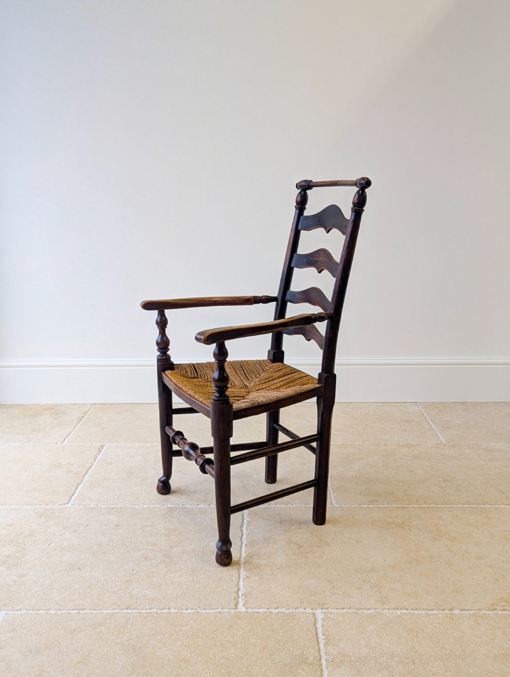 A late nineteenth-century country ash armchair featuring a ladderback design with four curved horizontal slats, turned armrest supports, and a hand-woven natural rush seat. View IX