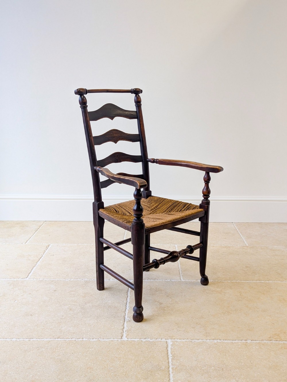 A late nineteenth-century country ash armchair featuring a ladderback design with four curved horizontal slats, turned armrest supports, and a hand-woven natural rush seat. View XI