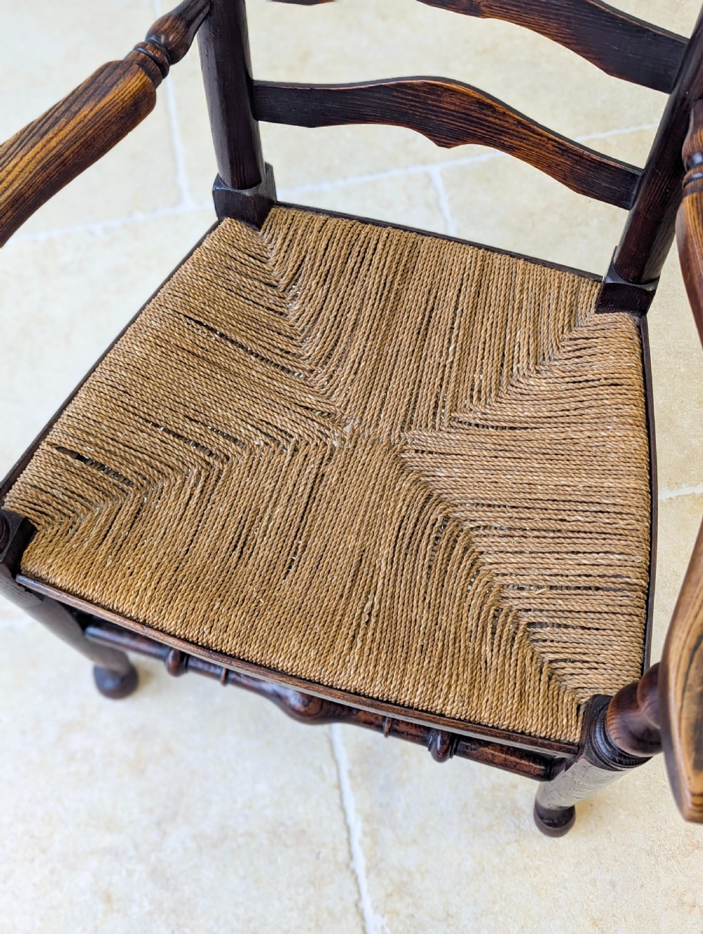 A late nineteenth-century country ash armchair featuring a ladderback design with four curved horizontal slats, turned armrest supports, and a hand-woven natural rush seat. View XII