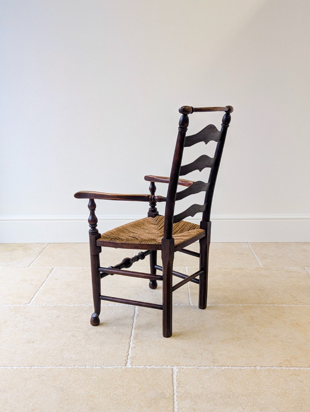 A late nineteenth-century country ash armchair featuring a ladderback design with four curved horizontal slats, turned armrest supports, and a hand-woven natural rush seat. View XIII