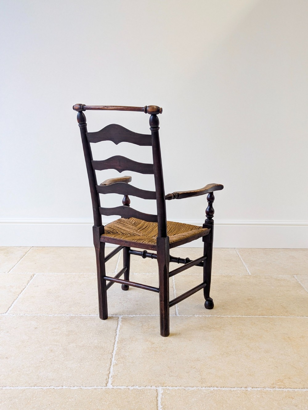 A late nineteenth-century country ash armchair featuring a ladderback design with four curved horizontal slats, turned armrest supports, and a hand-woven natural rush seat. View XIV