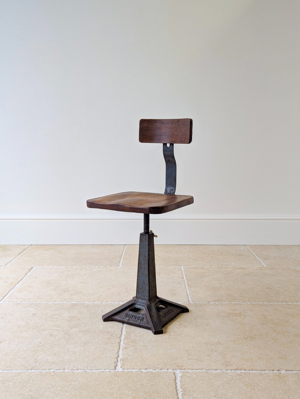 An early 20th-century Singer industrial chair featuring a dark cast iron pedestal base, a threaded height-adjustment mechanism, and a shaped elm seat with an attached wooden backrest.