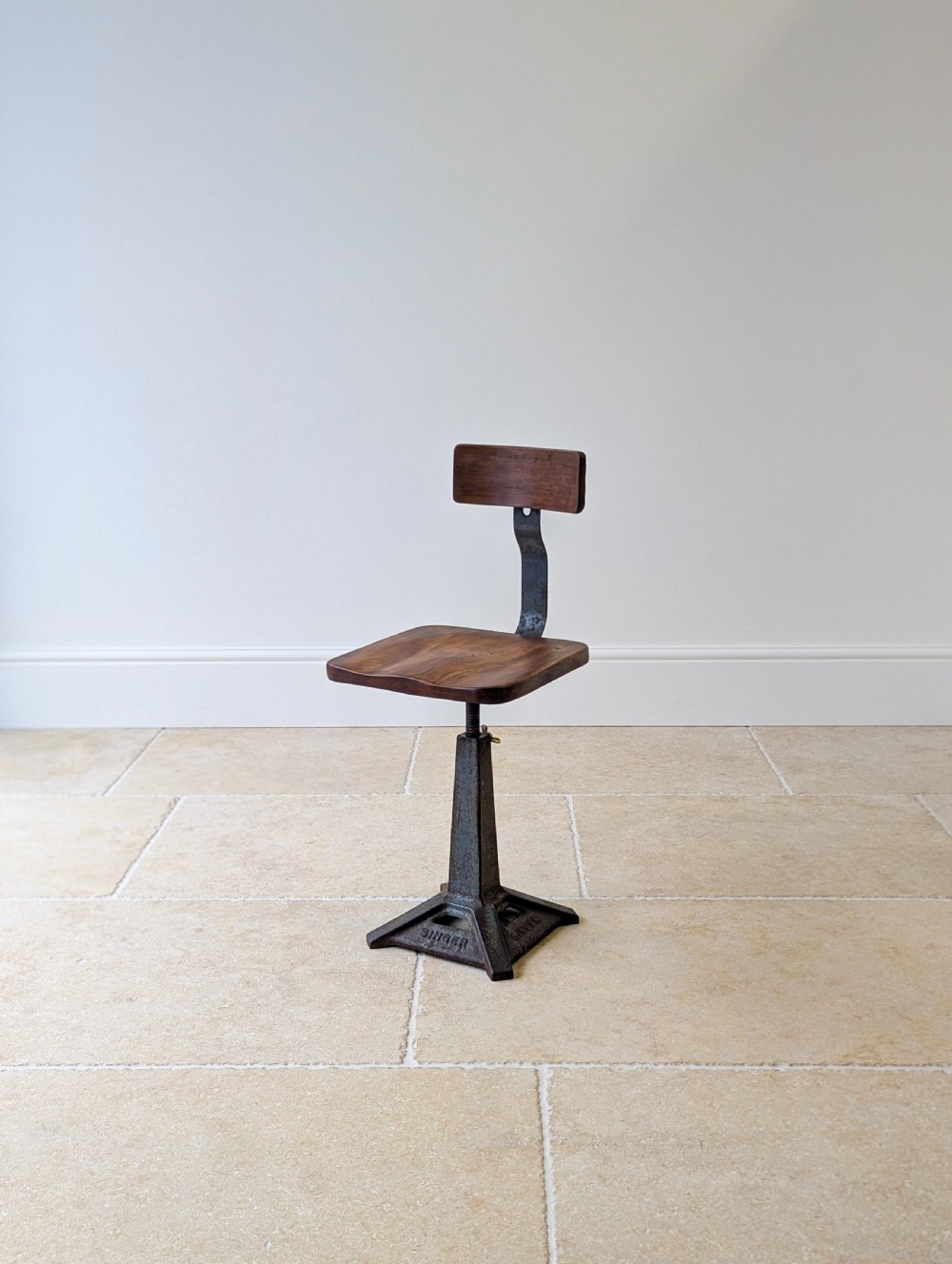 An early 20th-century Singer industrial chair featuring a dark cast iron pedestal base, a threaded height-adjustment mechanism, and a shaped elm seat with an attached wooden backrest. View V