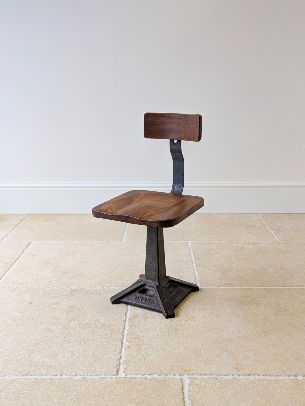 An early 20th-century Singer industrial chair featuring a dark cast iron pedestal base, a threaded height-adjustment mechanism, and a shaped elm seat with an attached wooden backrest. View VII