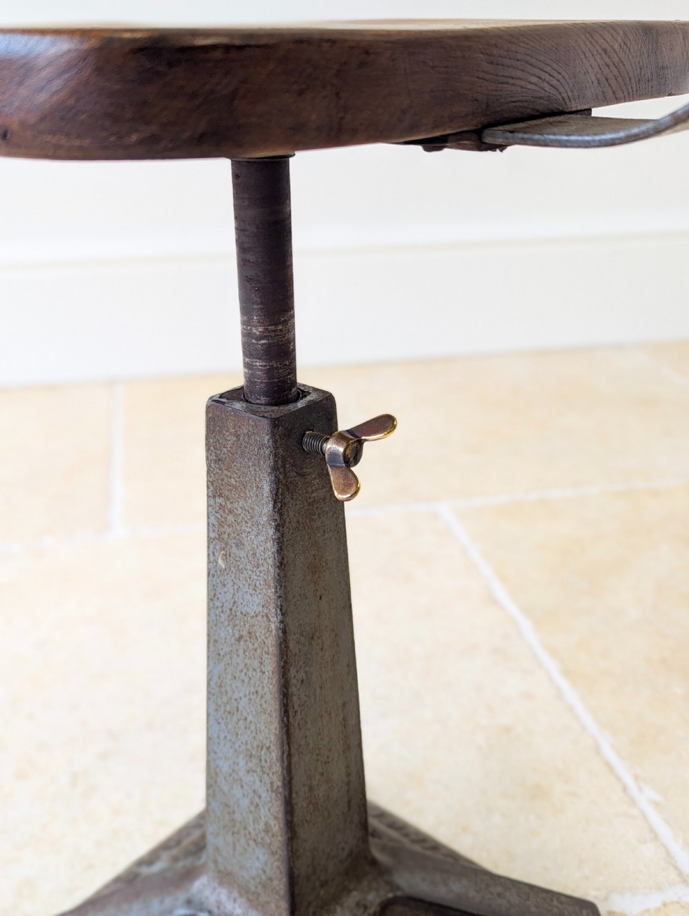 An early 20th-century Singer industrial chair featuring a dark cast iron pedestal base, a threaded height-adjustment mechanism, and a shaped elm seat with an attached wooden backrest. View VIII
