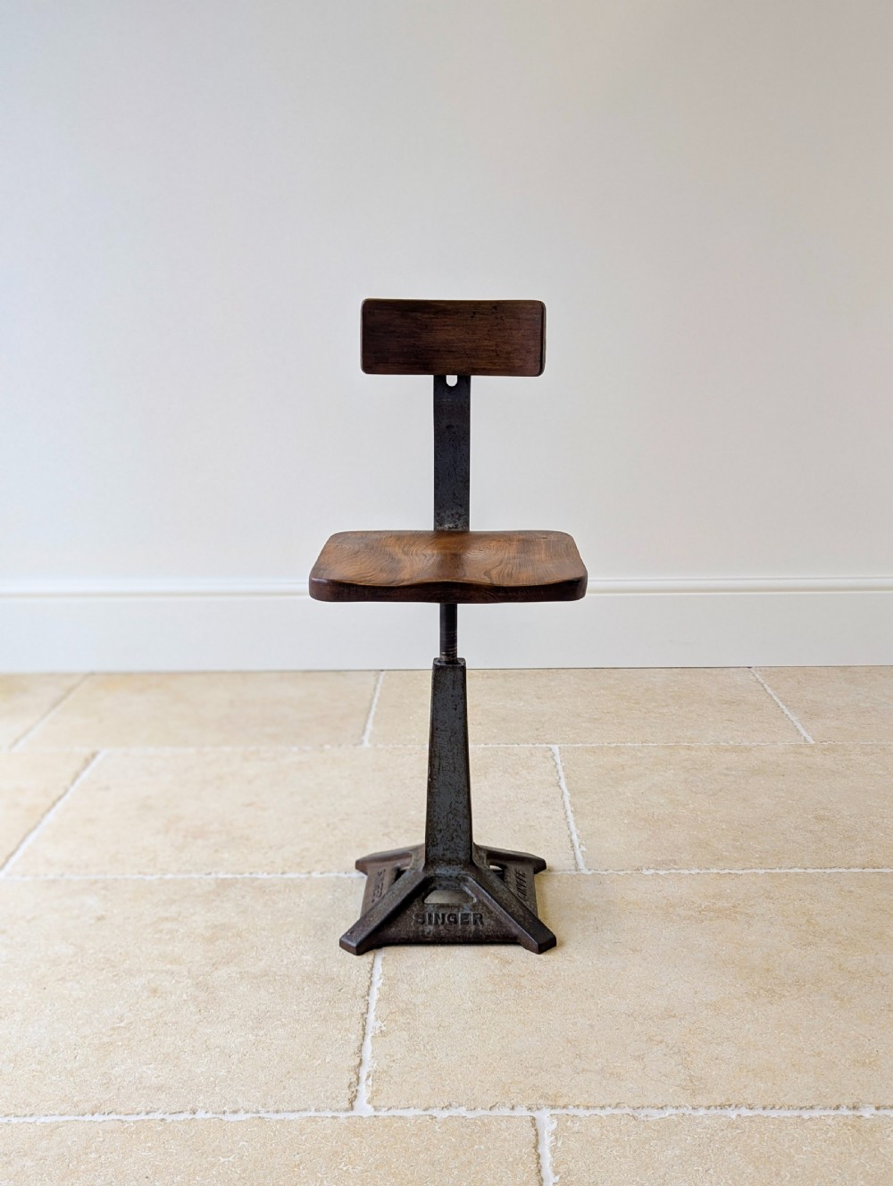 An early 20th-century Singer industrial chair featuring a dark cast iron pedestal base, a threaded height-adjustment mechanism, and a shaped elm seat with an attached wooden backrest. View IX