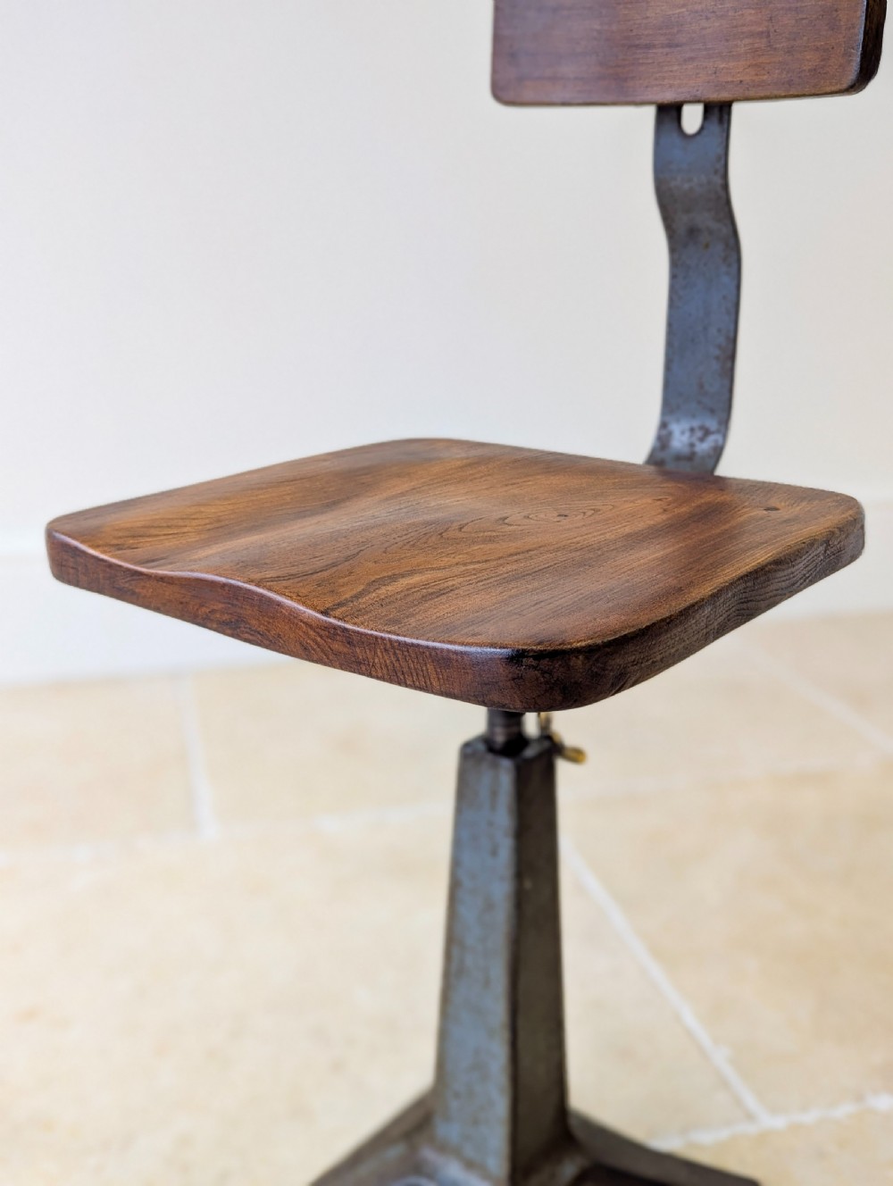 An early 20th-century Singer industrial chair featuring a dark cast iron pedestal base, a threaded height-adjustment mechanism, and a shaped elm seat with an attached wooden backrest. View X