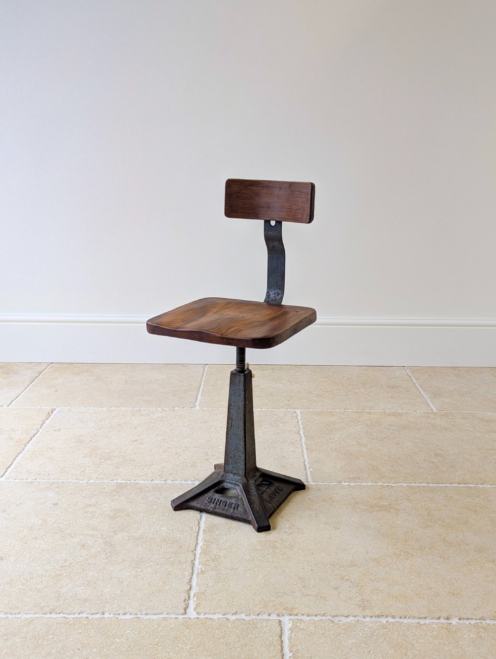An early 20th-century Singer industrial chair featuring a dark cast iron pedestal base, a threaded height-adjustment mechanism, and a shaped elm seat with an attached wooden backrest. View XI