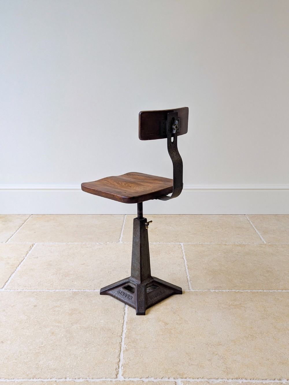 An early 20th-century Singer industrial chair featuring a dark cast iron pedestal base, a threaded height-adjustment mechanism, and a shaped elm seat with an attached wooden backrest. View XIV