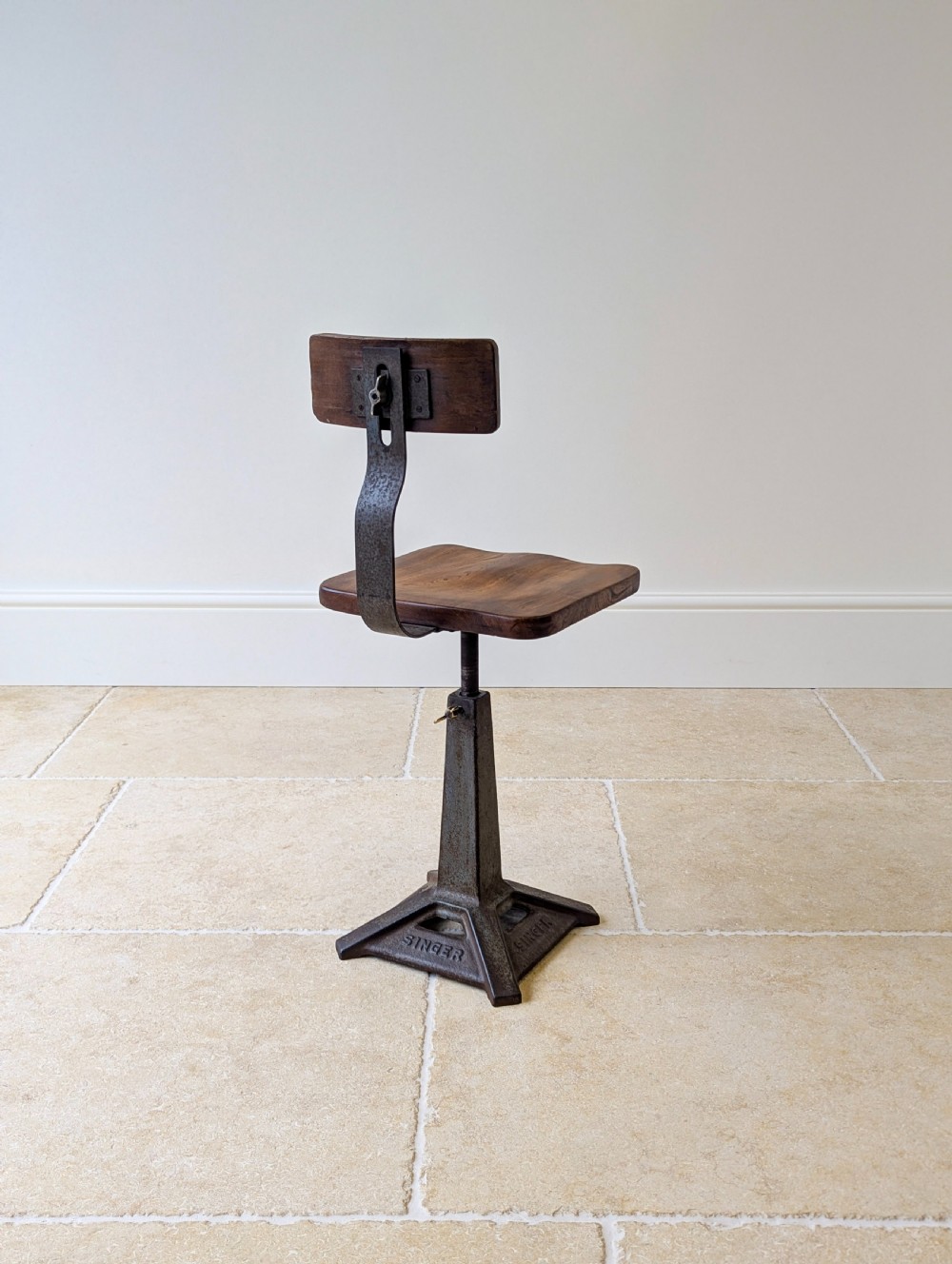 An early 20th-century Singer industrial chair featuring a dark cast iron pedestal base, a threaded height-adjustment mechanism, and a shaped elm seat with an attached wooden backrest. View XV