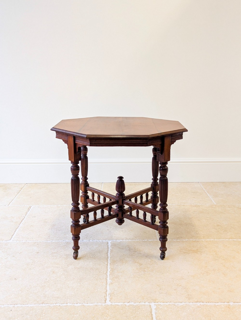 A late Victorian mahogany octagonal centre table featuring turned reeded legs, an intricate X-stretcher with baluster spindles, a central finial, and brass castors.