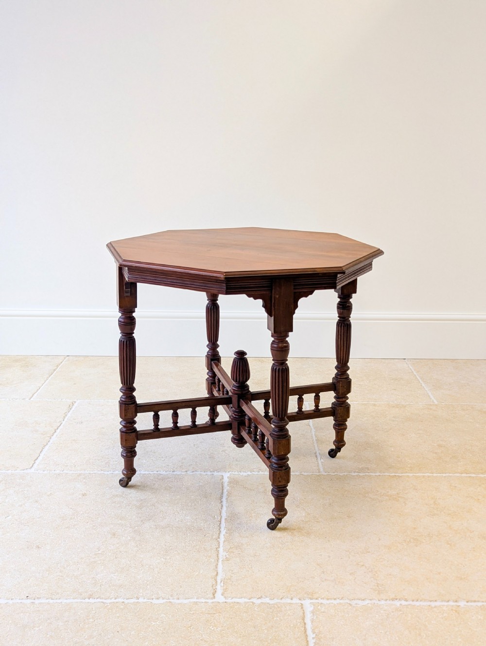A late Victorian mahogany octagonal centre table featuring turned reeded legs, an intricate X-stretcher with baluster spindles, a central finial, and brass castors. View II