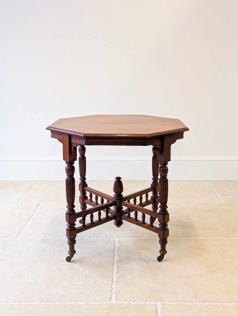 A late Victorian mahogany octagonal centre table featuring turned reeded legs, an intricate X-stretcher with baluster spindles, a central finial, and brass castors. View IV