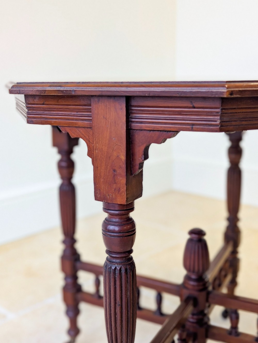 A late Victorian mahogany octagonal centre table featuring turned reeded legs, an intricate X-stretcher with baluster spindles, a central finial, and brass castors. View V
