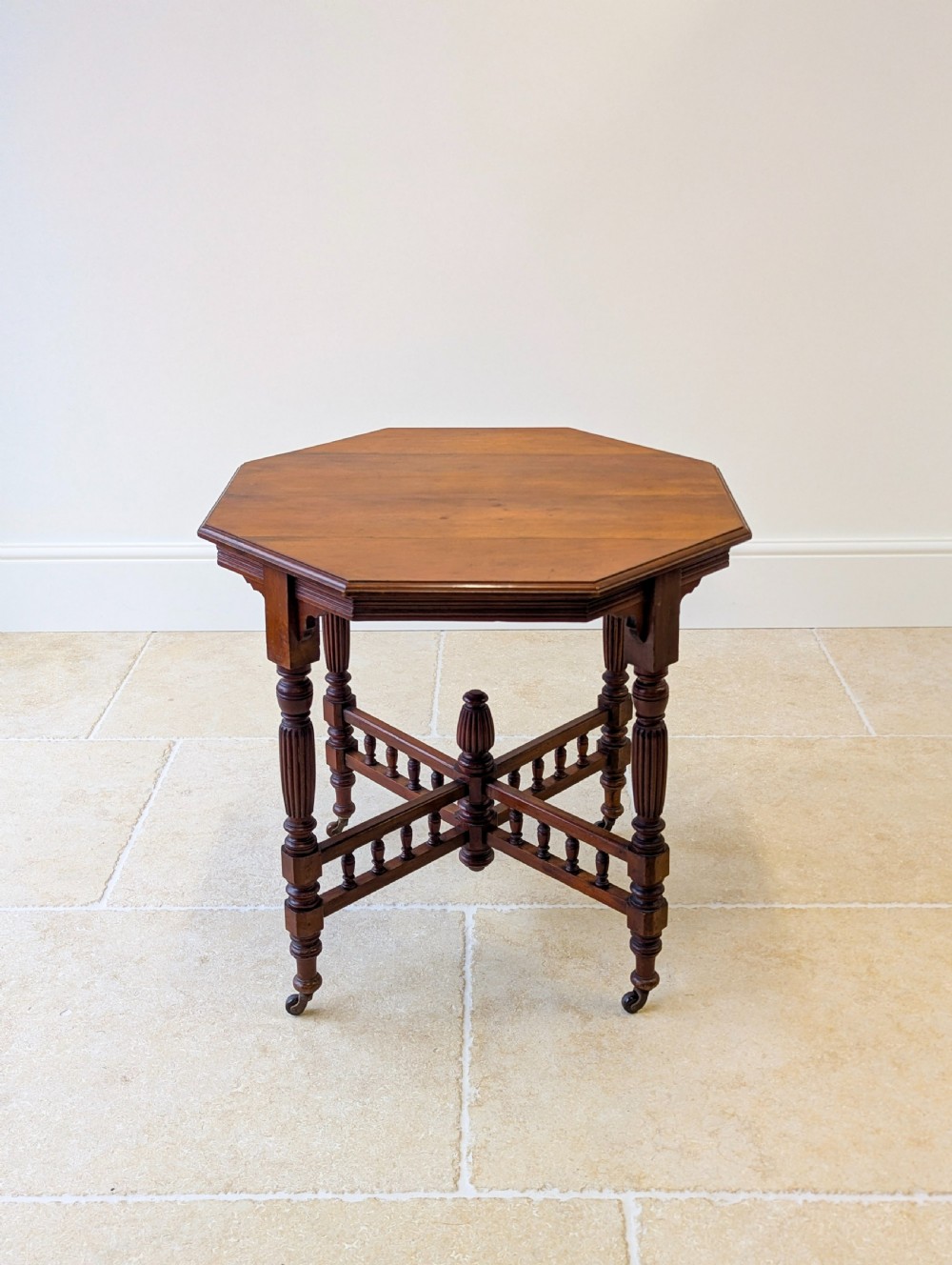 A late Victorian mahogany octagonal centre table featuring turned reeded legs, an intricate X-stretcher with baluster spindles, a central finial, and brass castors. View VI