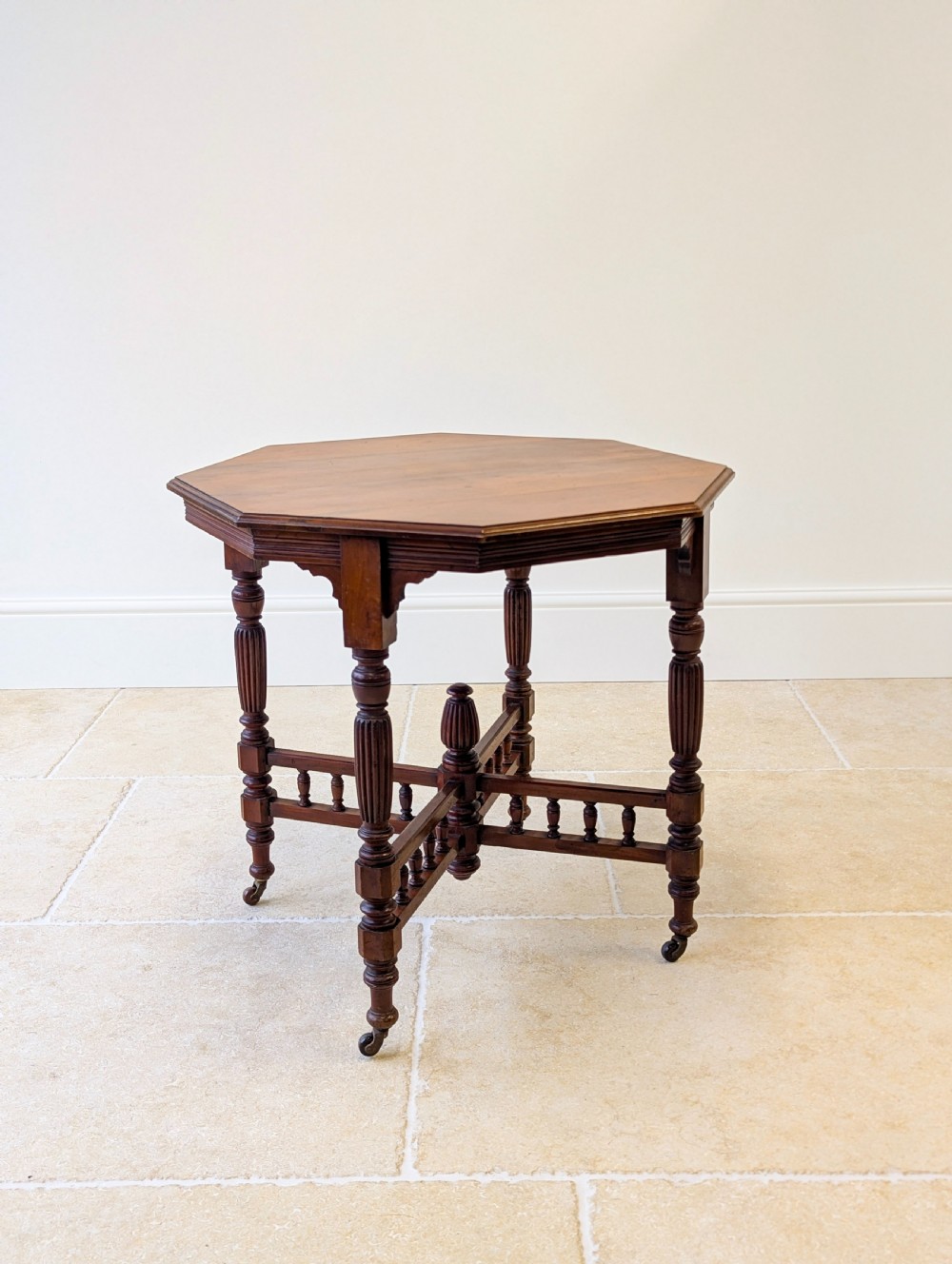 A late Victorian mahogany octagonal centre table featuring turned reeded legs, an intricate X-stretcher with baluster spindles, a central finial, and brass castors. View VIII