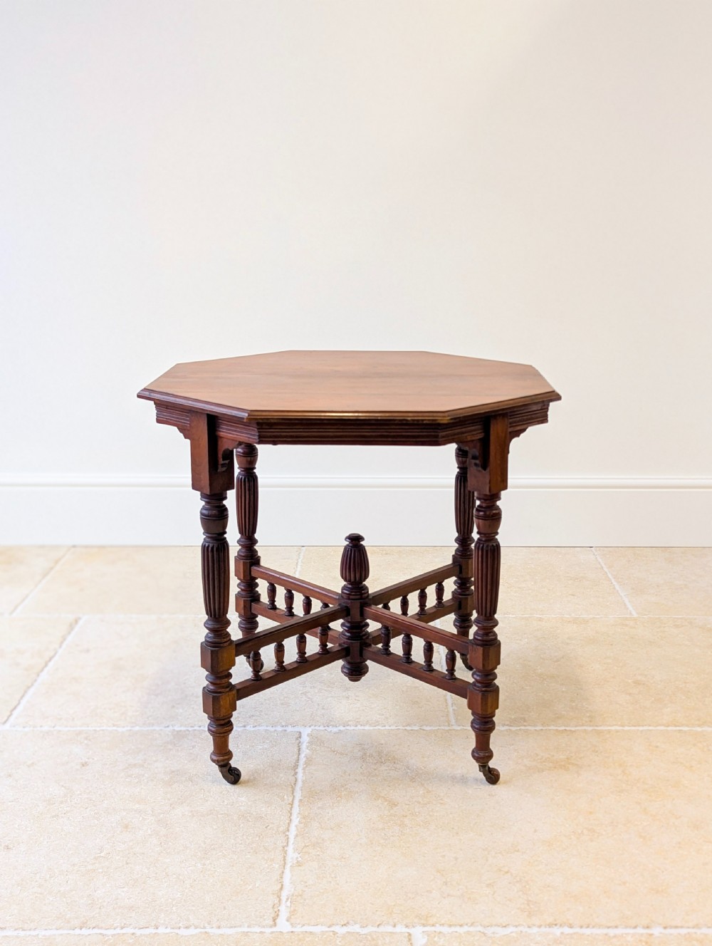 A late Victorian mahogany octagonal centre table featuring turned reeded legs, an intricate X-stretcher with baluster spindles, a central finial, and brass castors. View X