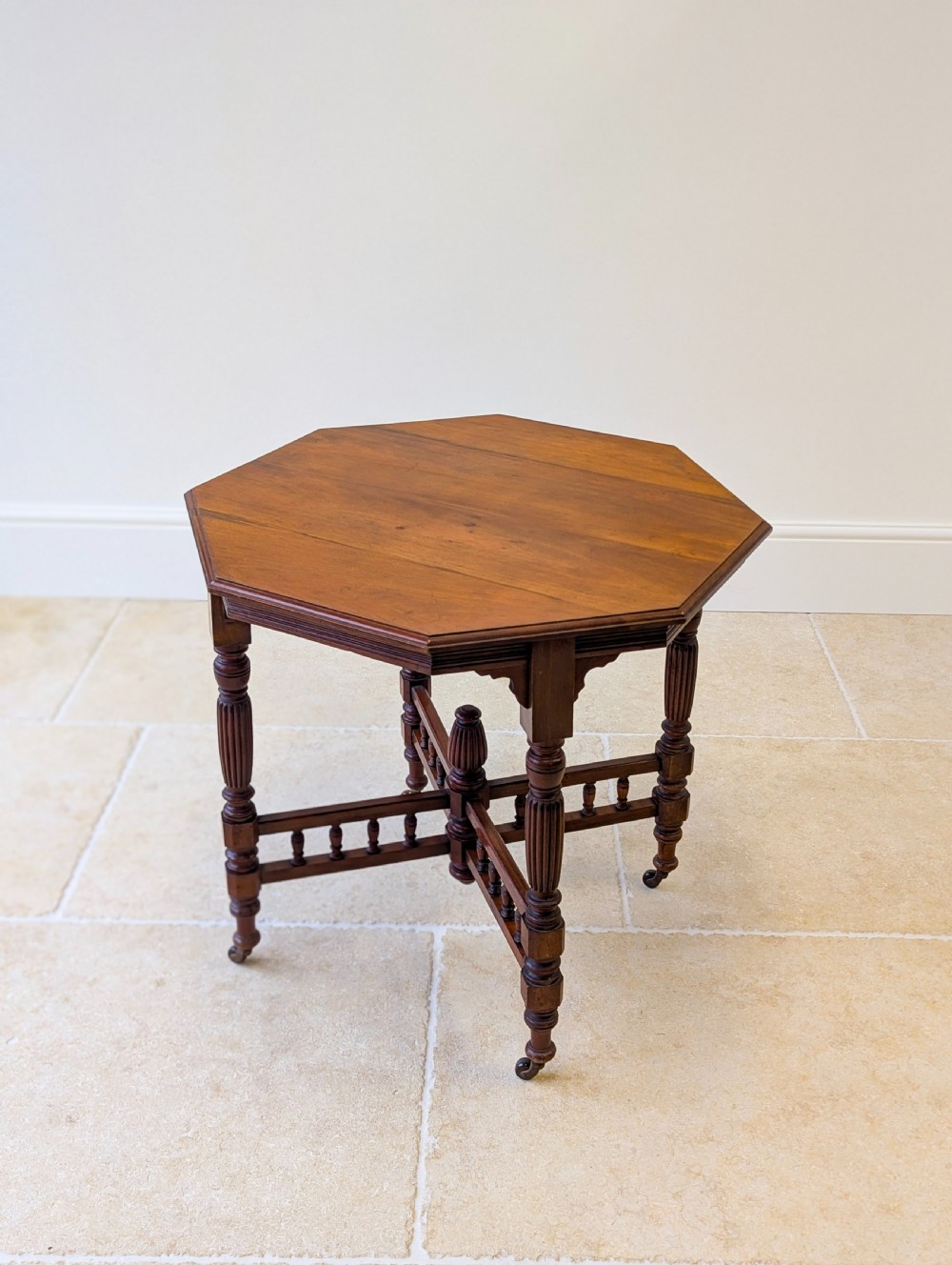 A late Victorian mahogany octagonal centre table featuring turned reeded legs, an intricate X-stretcher with baluster spindles, a central finial, and brass castors. View XII