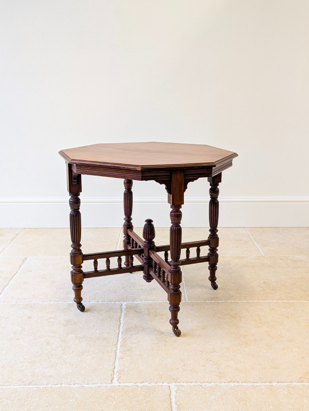 A late Victorian mahogany octagonal centre table featuring turned reeded legs, an intricate X-stretcher with baluster spindles, a central finial, and brass castors. View XIV