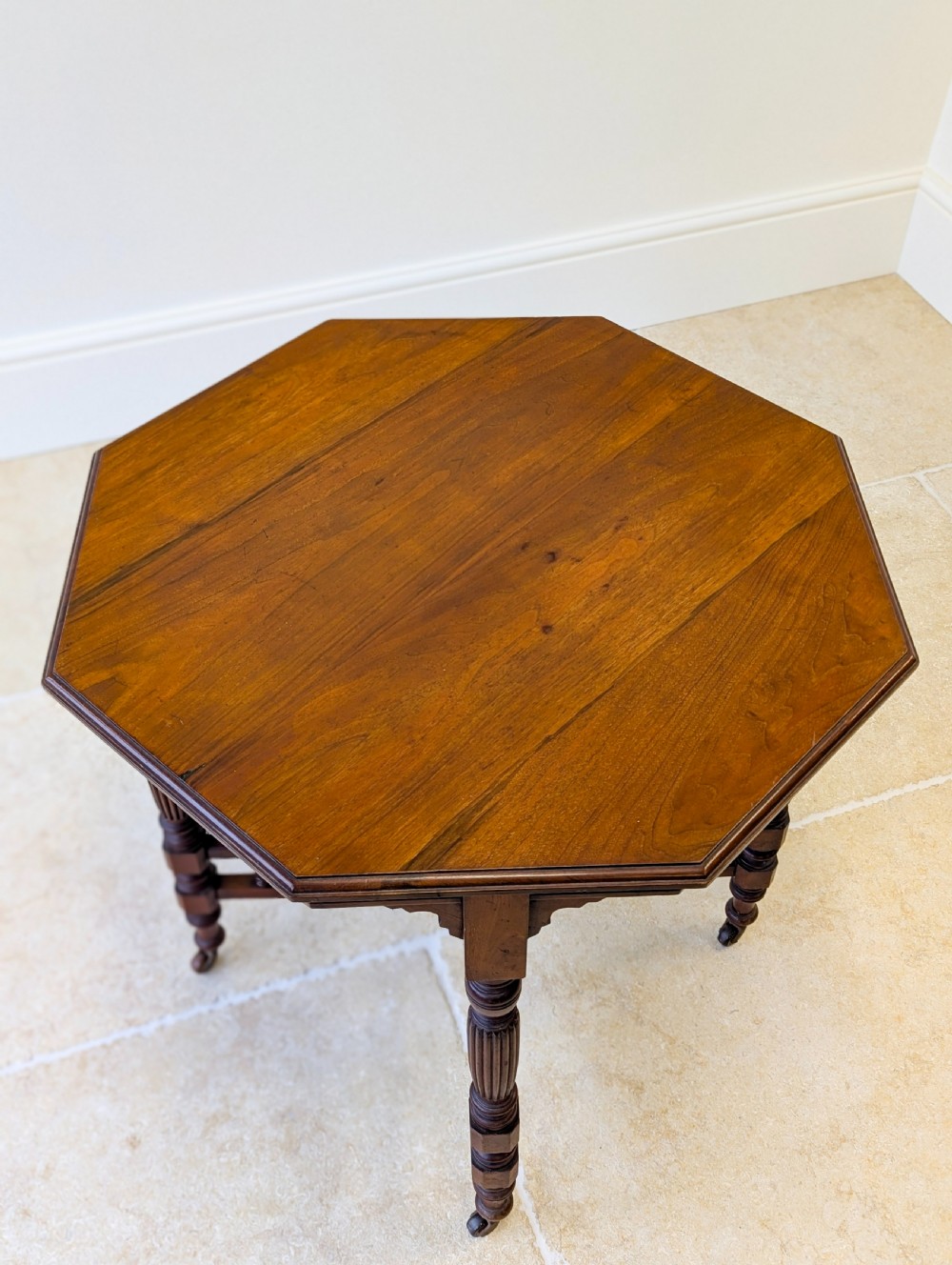 A late Victorian mahogany octagonal centre table featuring turned reeded legs, an intricate X-stretcher with baluster spindles, a central finial, and brass castors. View XV