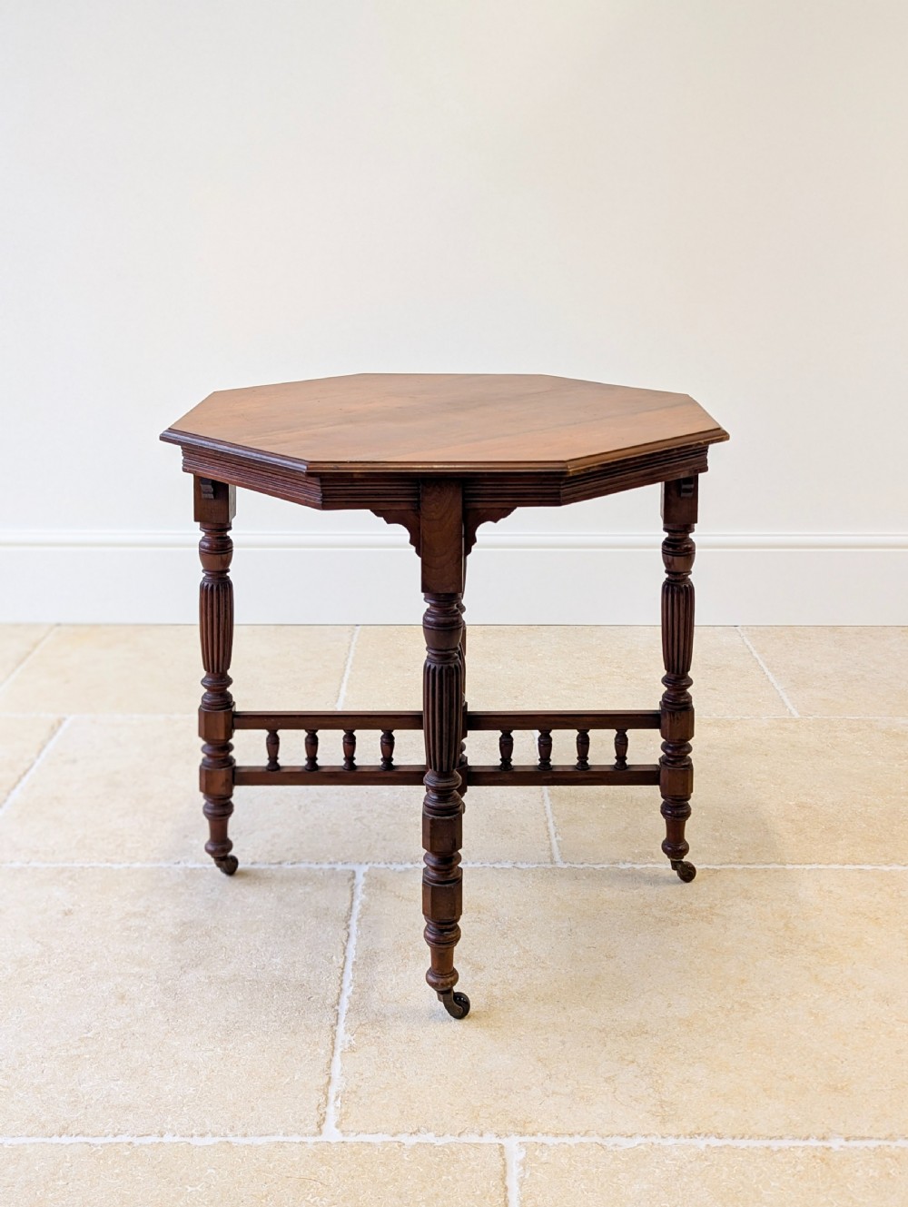 A late Victorian mahogany octagonal centre table featuring turned reeded legs, an intricate X-stretcher with baluster spindles, a central finial, and brass castors. View XVI