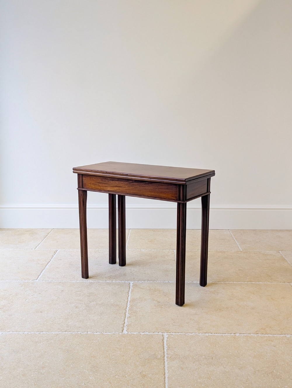 A late 18th-century dark mahogany fold-over tea table featuring reeded straight legs and a polished hinged top.