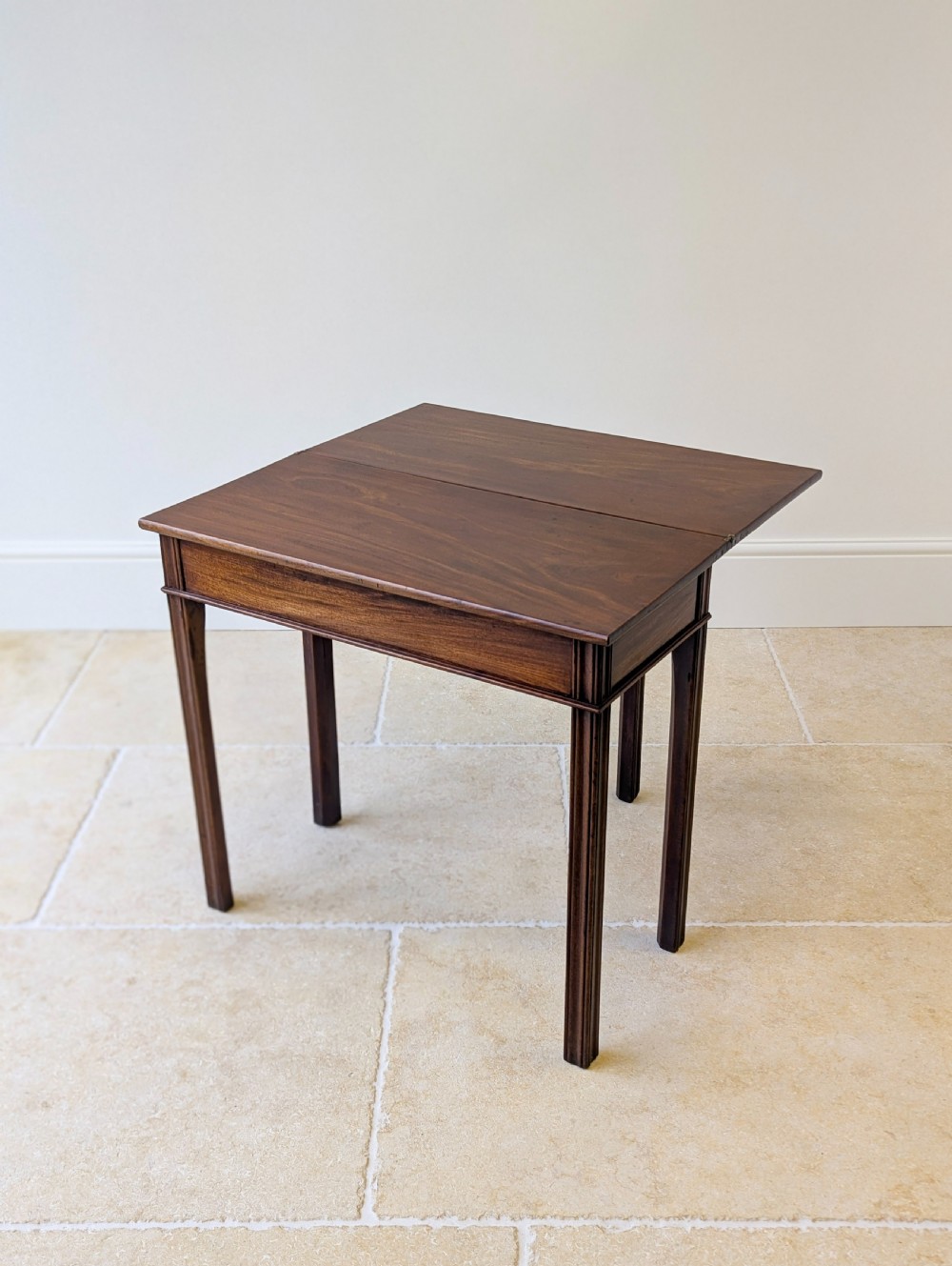 A late 18th-century dark mahogany fold-over tea table featuring reeded straight legs and a polished hinged top. View V