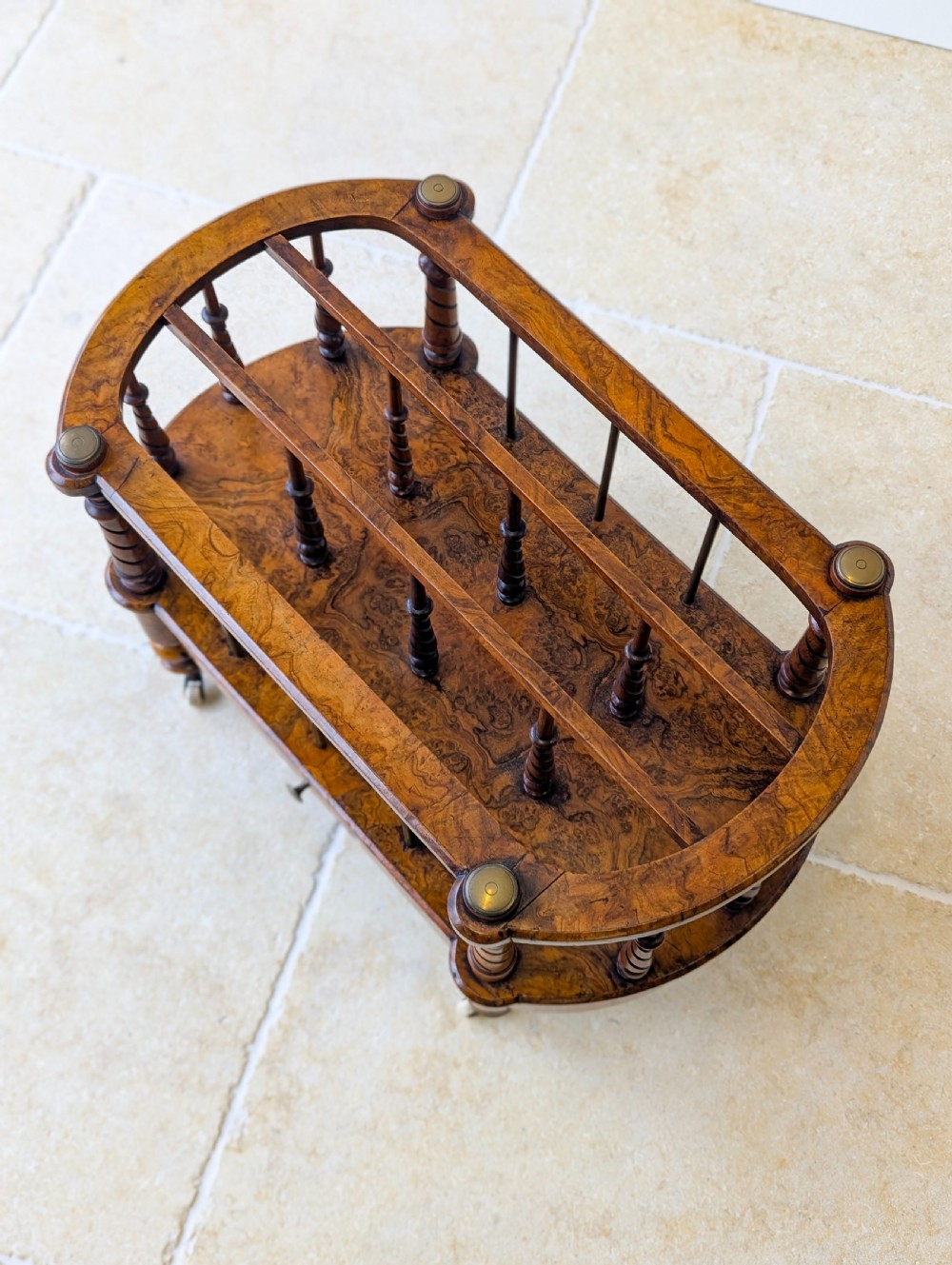 A Victorian burr walnut canterbury featuring turned spiral columns, brass division rods, a base drawer, and ceramic castors. View II