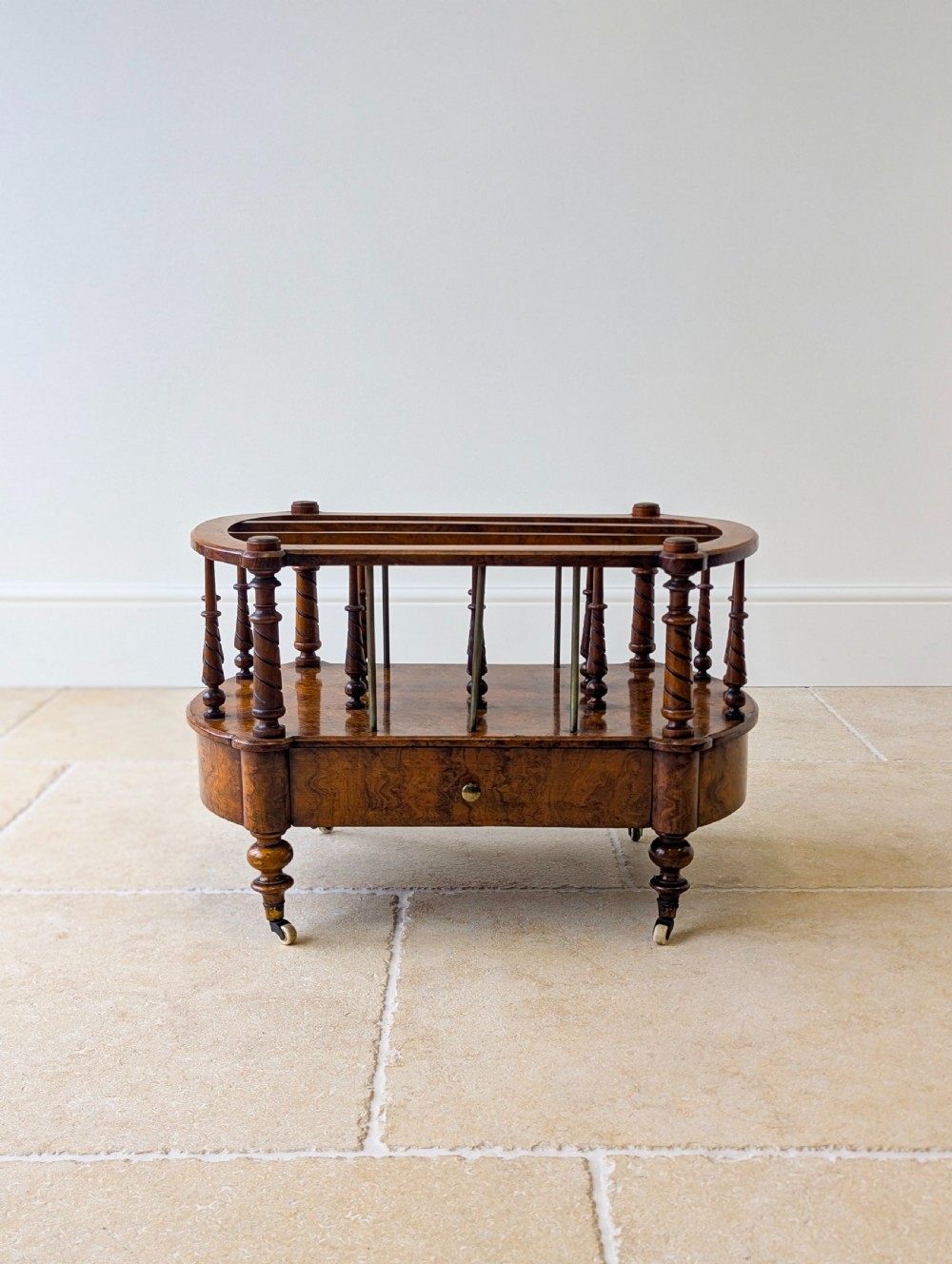 A Victorian burr walnut canterbury featuring turned spiral columns, brass division rods, a base drawer, and ceramic castors. View III