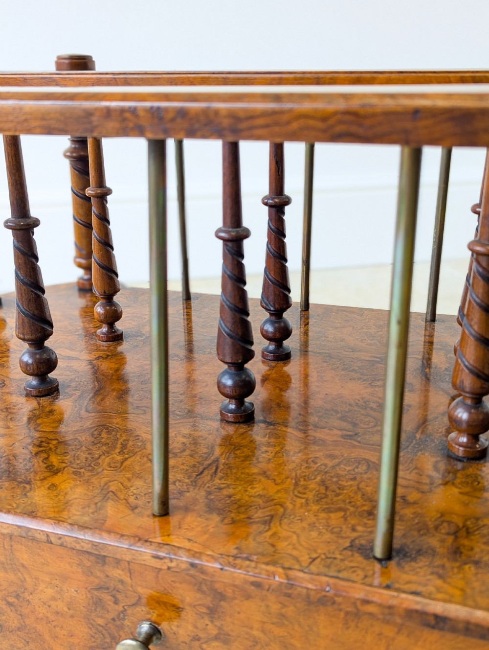A Victorian burr walnut canterbury featuring turned spiral columns, brass division rods, a base drawer, and ceramic castors. View IV