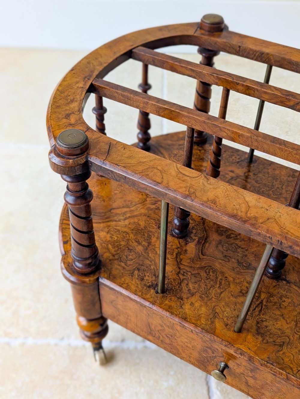 A Victorian burr walnut canterbury featuring turned spiral columns, brass division rods, a base drawer, and ceramic castors. View VI