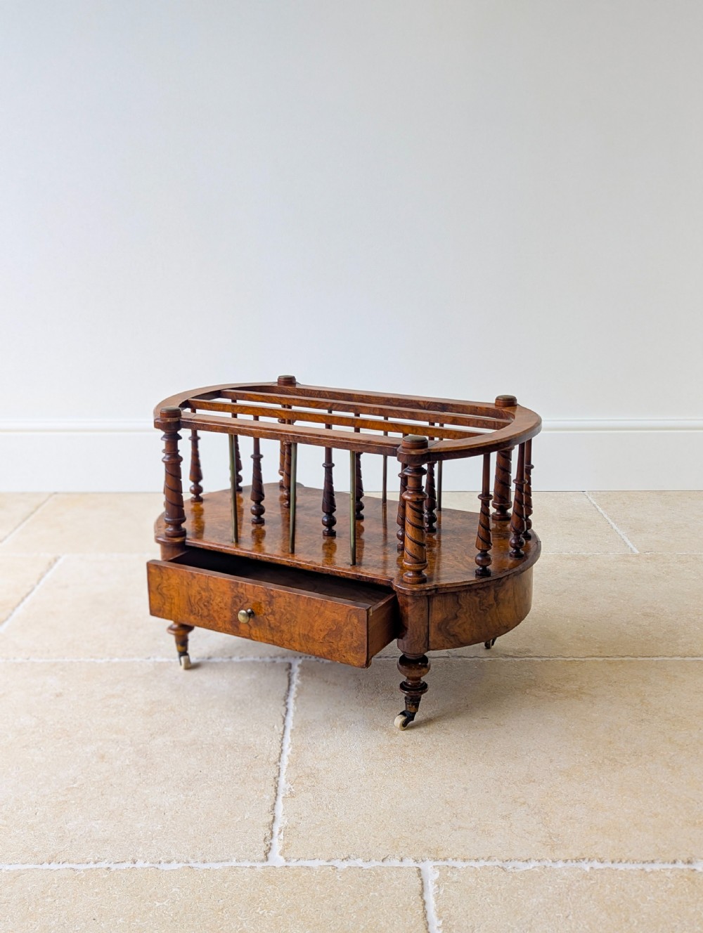 A Victorian burr walnut canterbury featuring turned spiral columns, brass division rods, a base drawer, and ceramic castors. View VII
