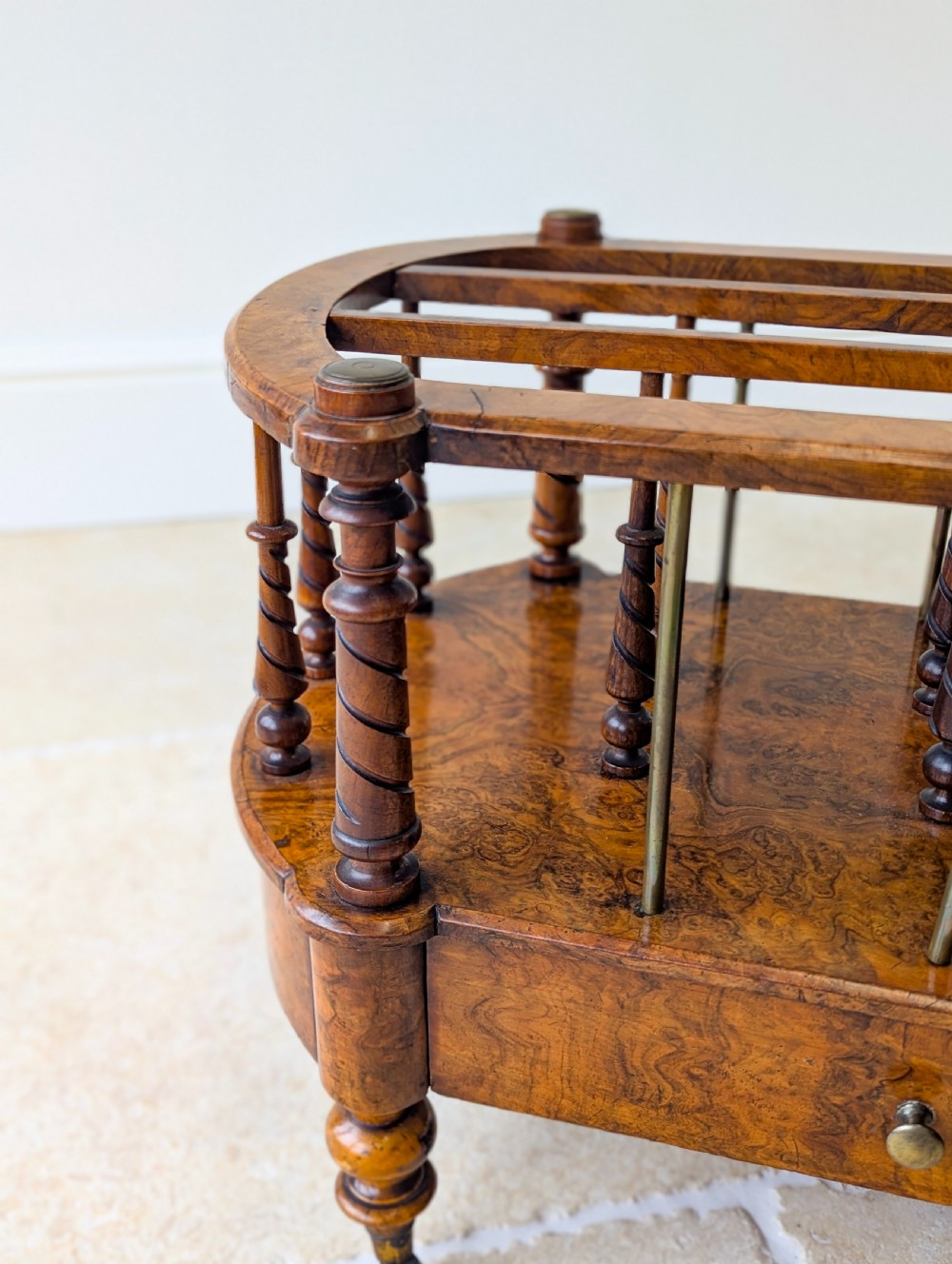 A Victorian burr walnut canterbury featuring turned spiral columns, brass division rods, a base drawer, and ceramic castors. View VIII