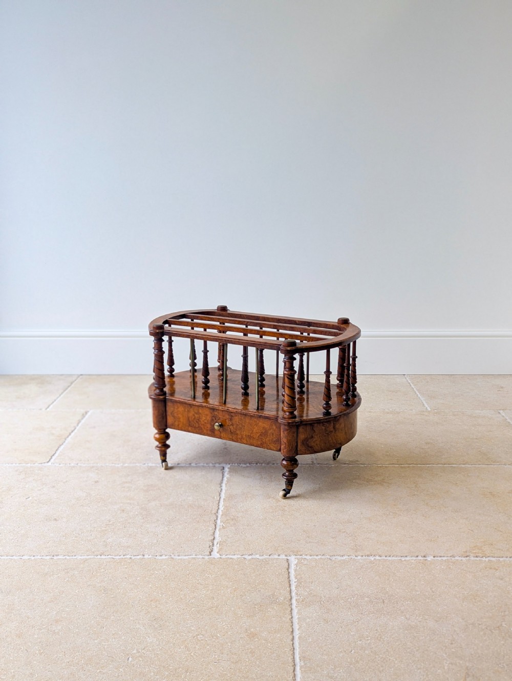 A Victorian burr walnut canterbury featuring turned spiral columns, brass division rods, a base drawer, and ceramic castors. View IX