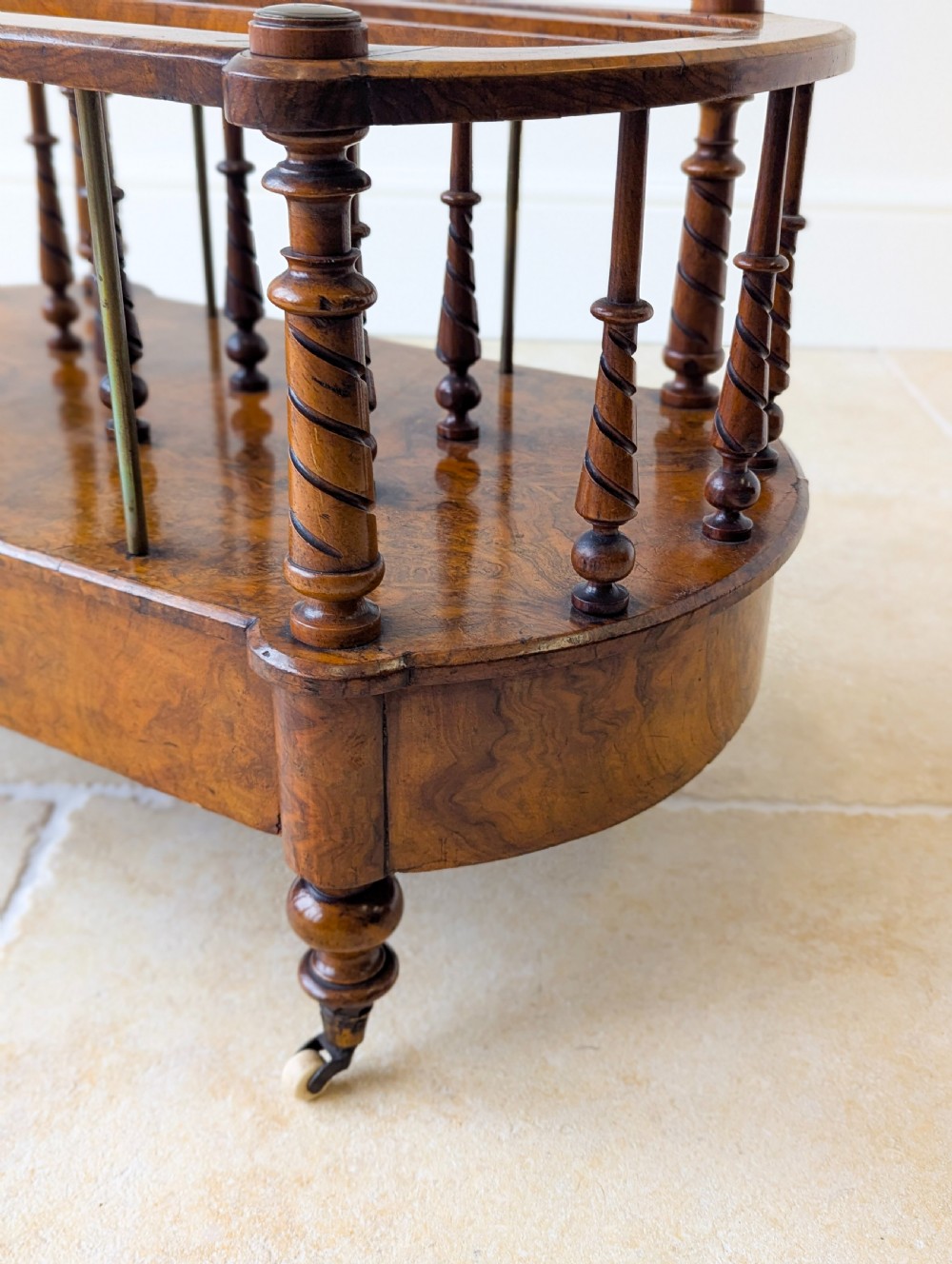 A Victorian burr walnut canterbury featuring turned spiral columns, brass division rods, a base drawer, and ceramic castors. View X