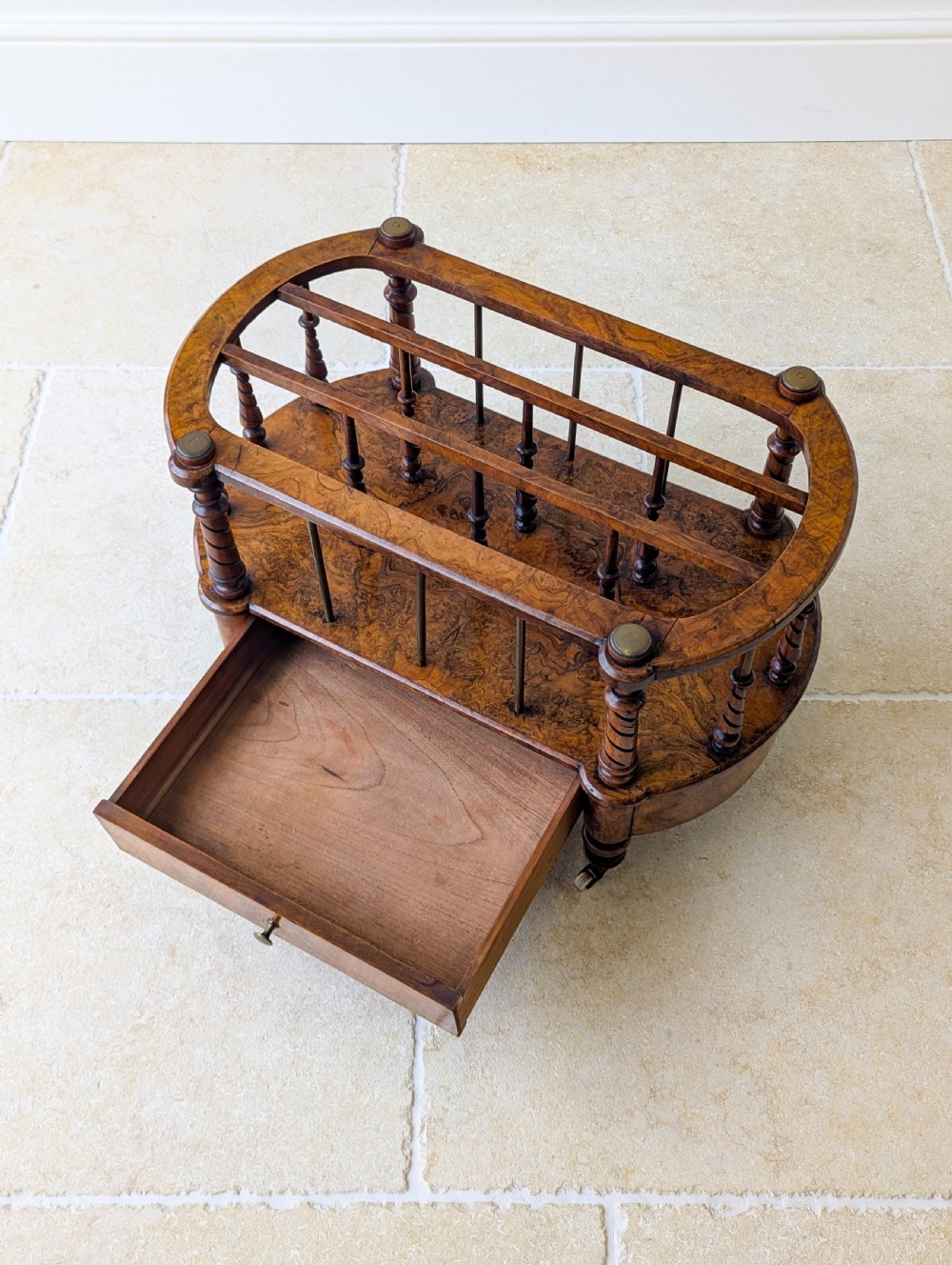 A Victorian burr walnut canterbury featuring turned spiral columns, brass division rods, a base drawer, and ceramic castors. View XI