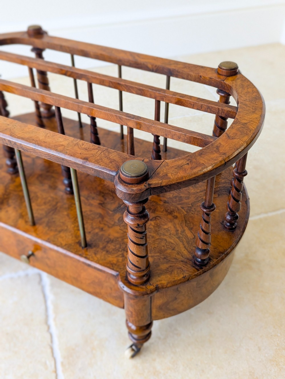 A Victorian burr walnut canterbury featuring turned spiral columns, brass division rods, a base drawer, and ceramic castors. View XII