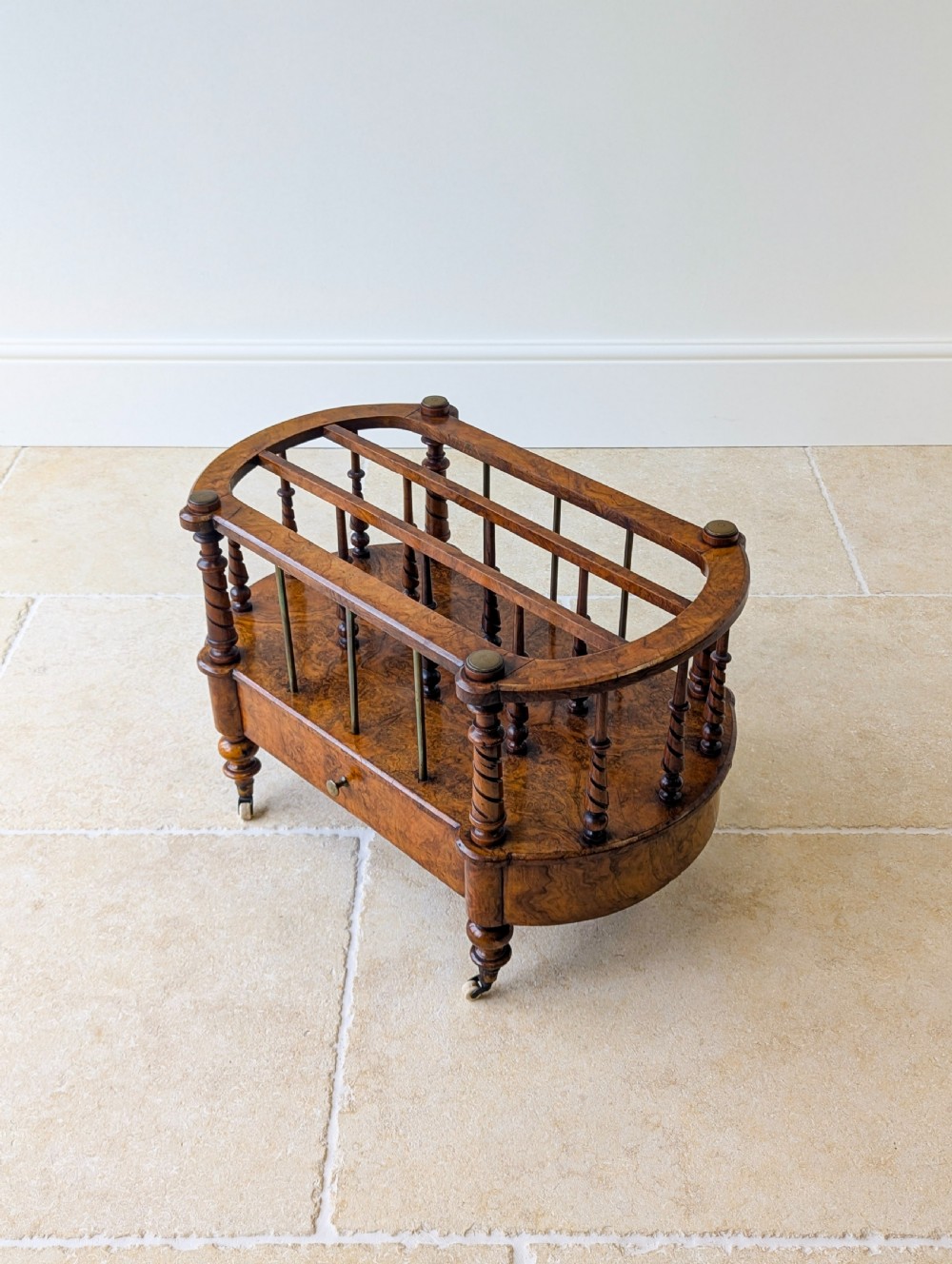 A Victorian burr walnut canterbury featuring turned spiral columns, brass division rods, a base drawer, and ceramic castors. View XIII