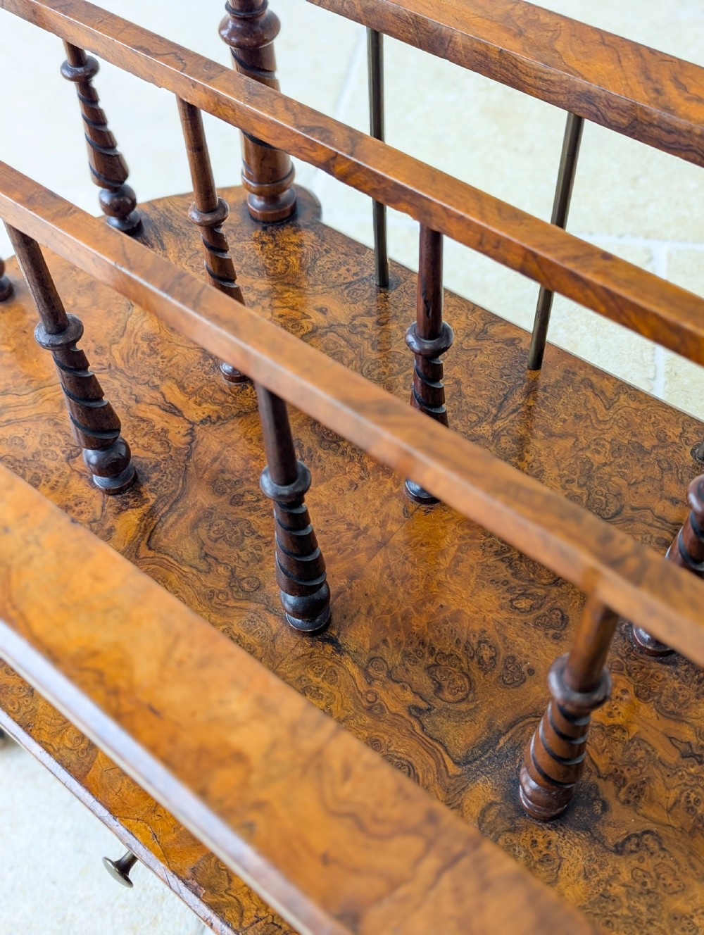 A Victorian burr walnut canterbury featuring turned spiral columns, brass division rods, a base drawer, and ceramic castors. View XIV