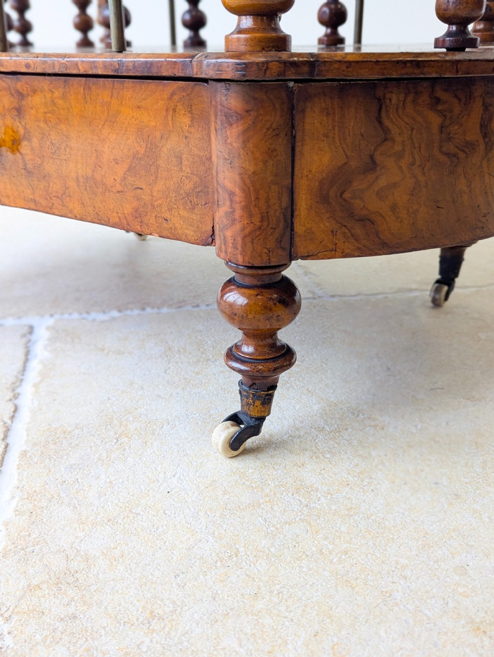 A Victorian burr walnut canterbury featuring turned spiral columns, brass division rods, a base drawer, and ceramic castors. View XVI