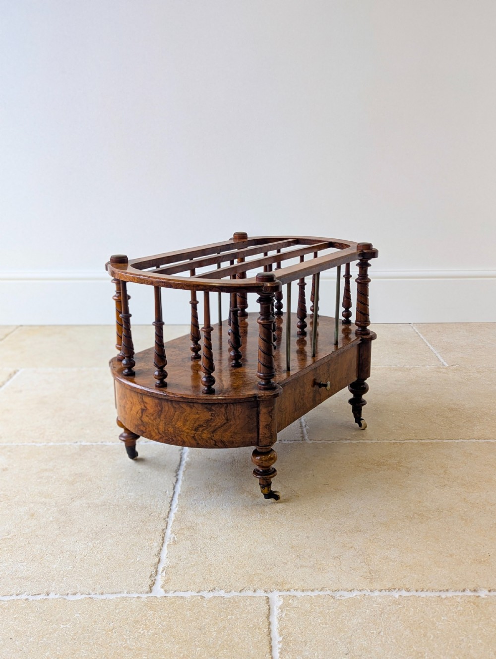 A Victorian burr walnut canterbury featuring turned spiral columns, brass division rods, a base drawer, and ceramic castors. View XVII
