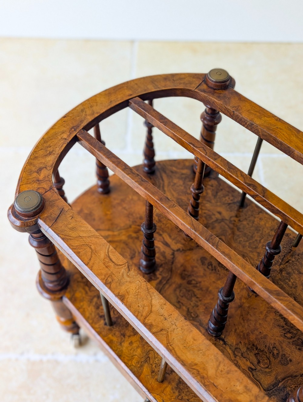 A Victorian burr walnut canterbury featuring turned spiral columns, brass division rods, a base drawer, and ceramic castors. View XVIII