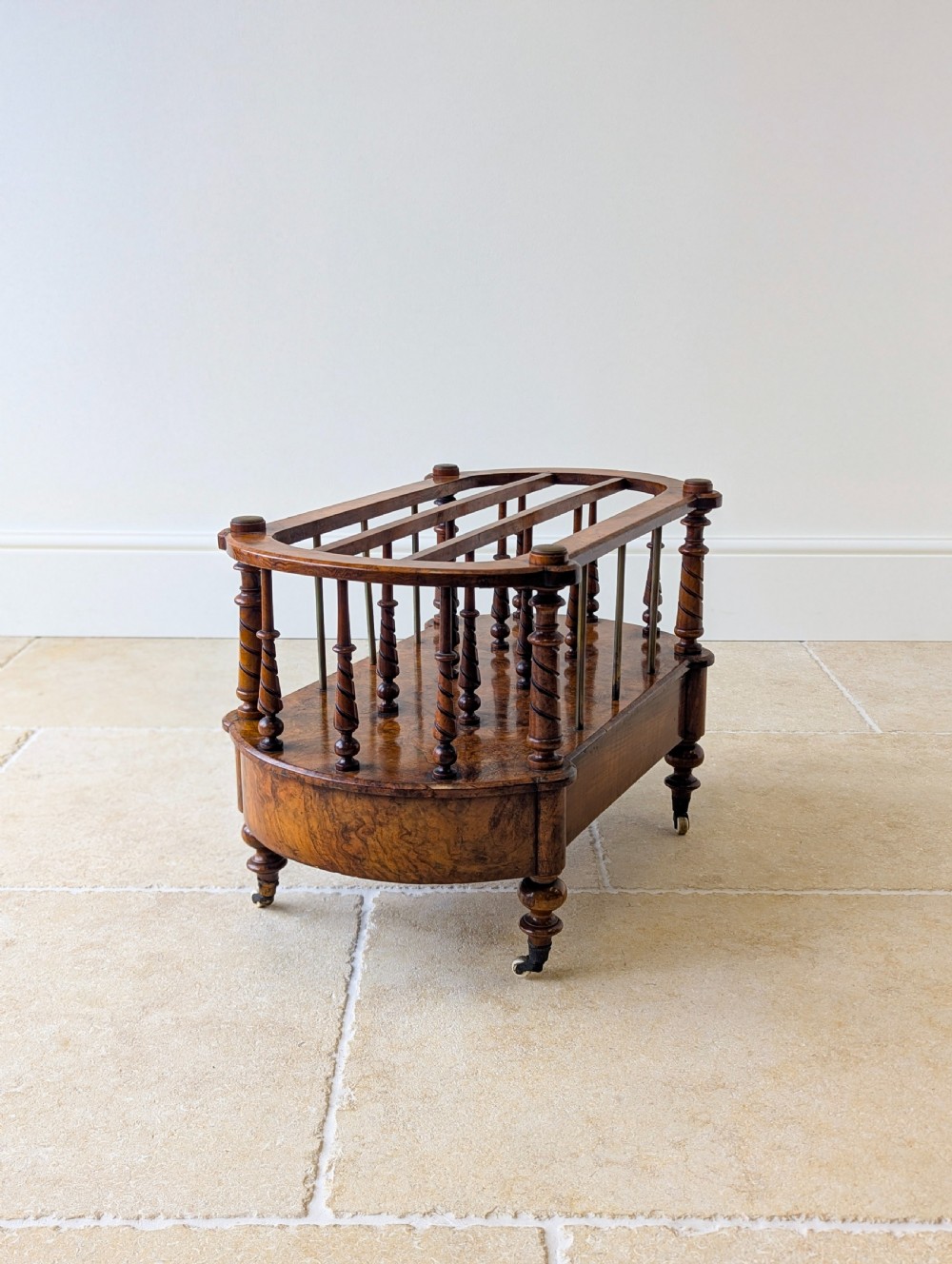 A Victorian burr walnut canterbury featuring turned spiral columns, brass division rods, a base drawer, and ceramic castors. View XIX