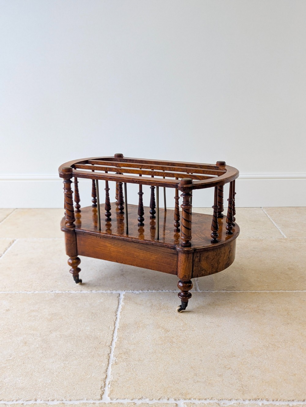 A Victorian burr walnut canterbury featuring turned spiral columns, brass division rods, a base drawer, and ceramic castors. View XX